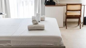 A hotel room with a neatly made bed, a wooden chair, and a desk with a coffee maker.