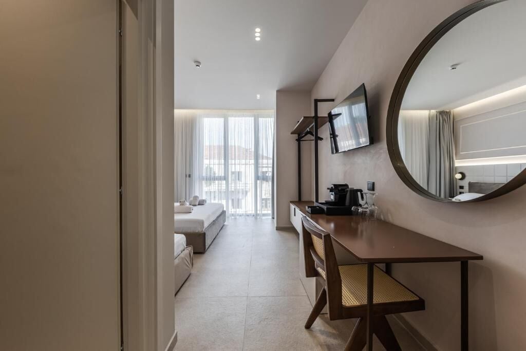 A hotel room with a bed, a desk, a chair, a television, and a large mirror.