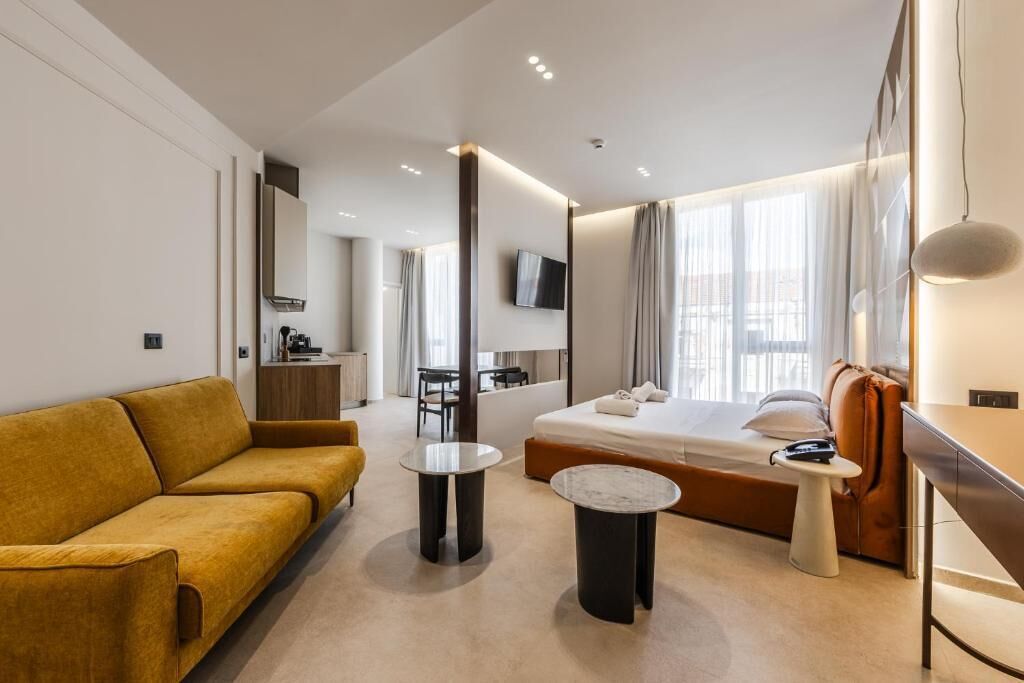 A modern hotel room with a sofa, a bed, a desk, and a TV.