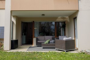 A modern outdoor seating area with a sofa and a table, a sliding glass door, and a small garden.