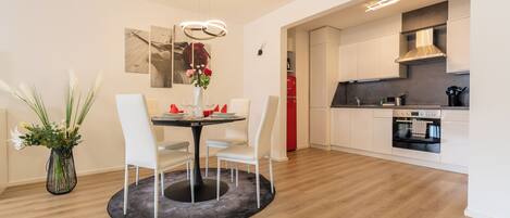 A modern kitchen with white cabinets, a built-in oven, and a dining area with a round table and white chairs.