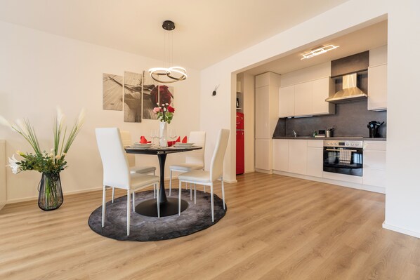 A modern kitchen with white cabinets, a built-in oven, and a dining area with a round table and white chairs.