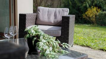 An outdoor seating area with a wicker sofa, a glass-top coffee table, and a potted plant.