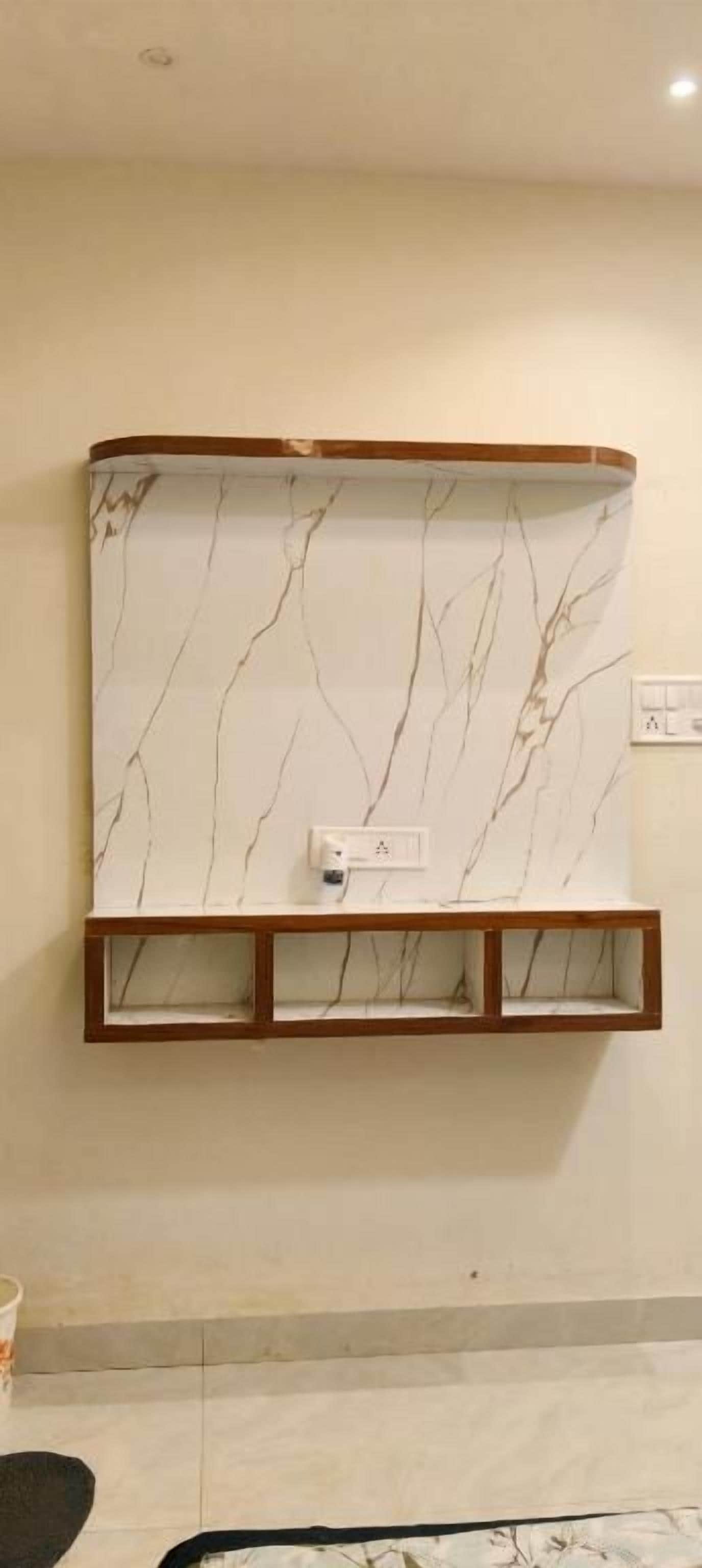 Un televisor de pared con diseño de mármol, un estante de madera debajo y un enchufe a la derecha.