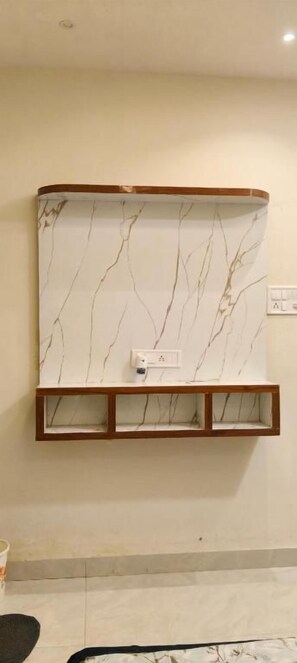 Un televisor de pared con diseño de mármol, un estante de madera debajo y un enchufe a la derecha.