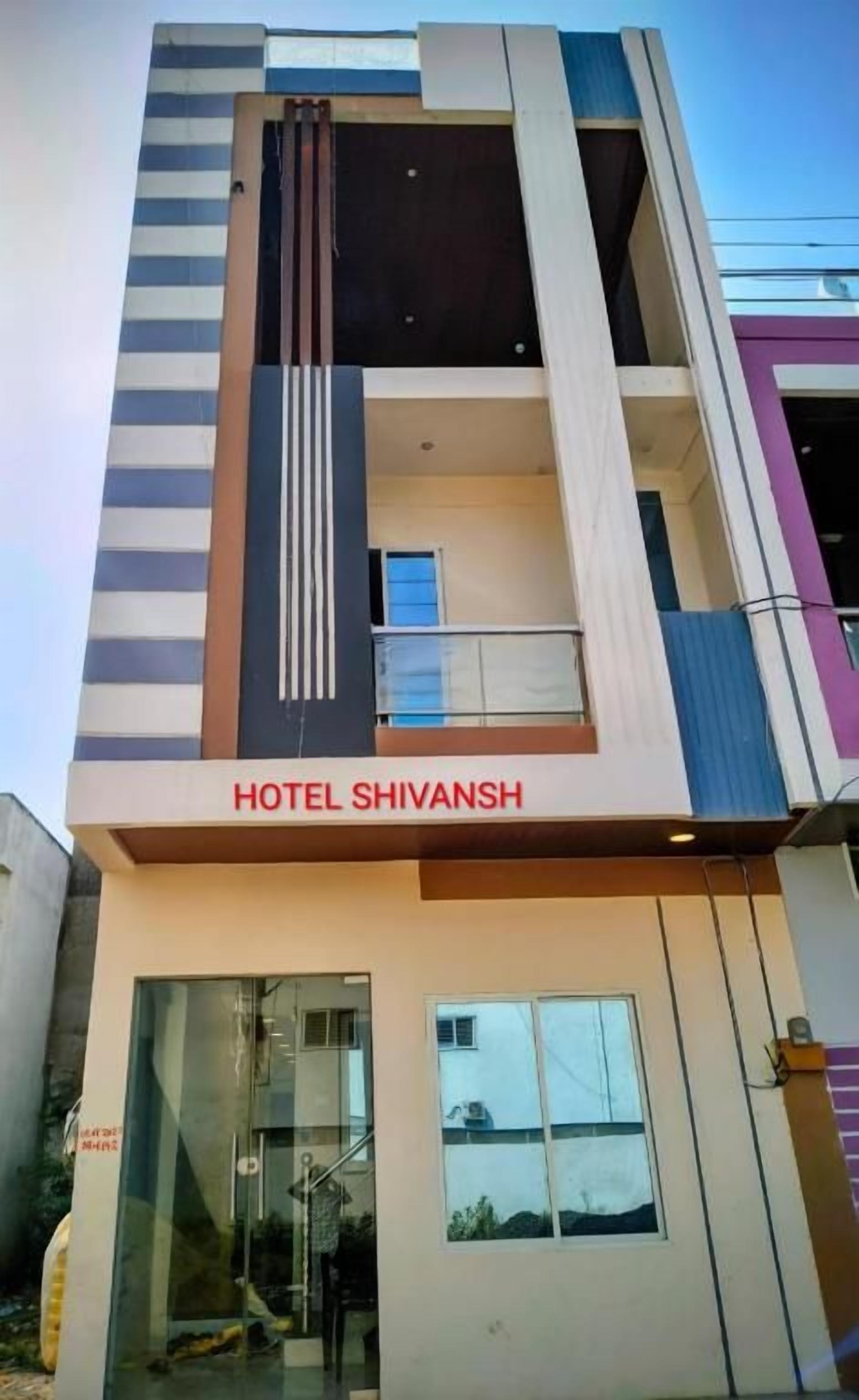 Un hotel llamado 'HOTEL SHIVANSH' con una fachada moderna, una entrada de vidrio y un balcón visible.
