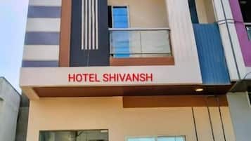 Un hotel llamado 'HOTEL SHIVANSH' con una fachada moderna, una entrada de vidrio y un balcón visible.