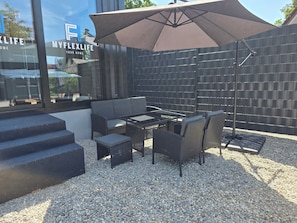 An outdoor patio area with a sofa, table, chairs, and a large umbrella.