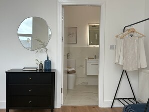 Una habitació amb un taulell negre, un mirall rodó, una estant per a la roba penjada i una porta que dona a un bany.