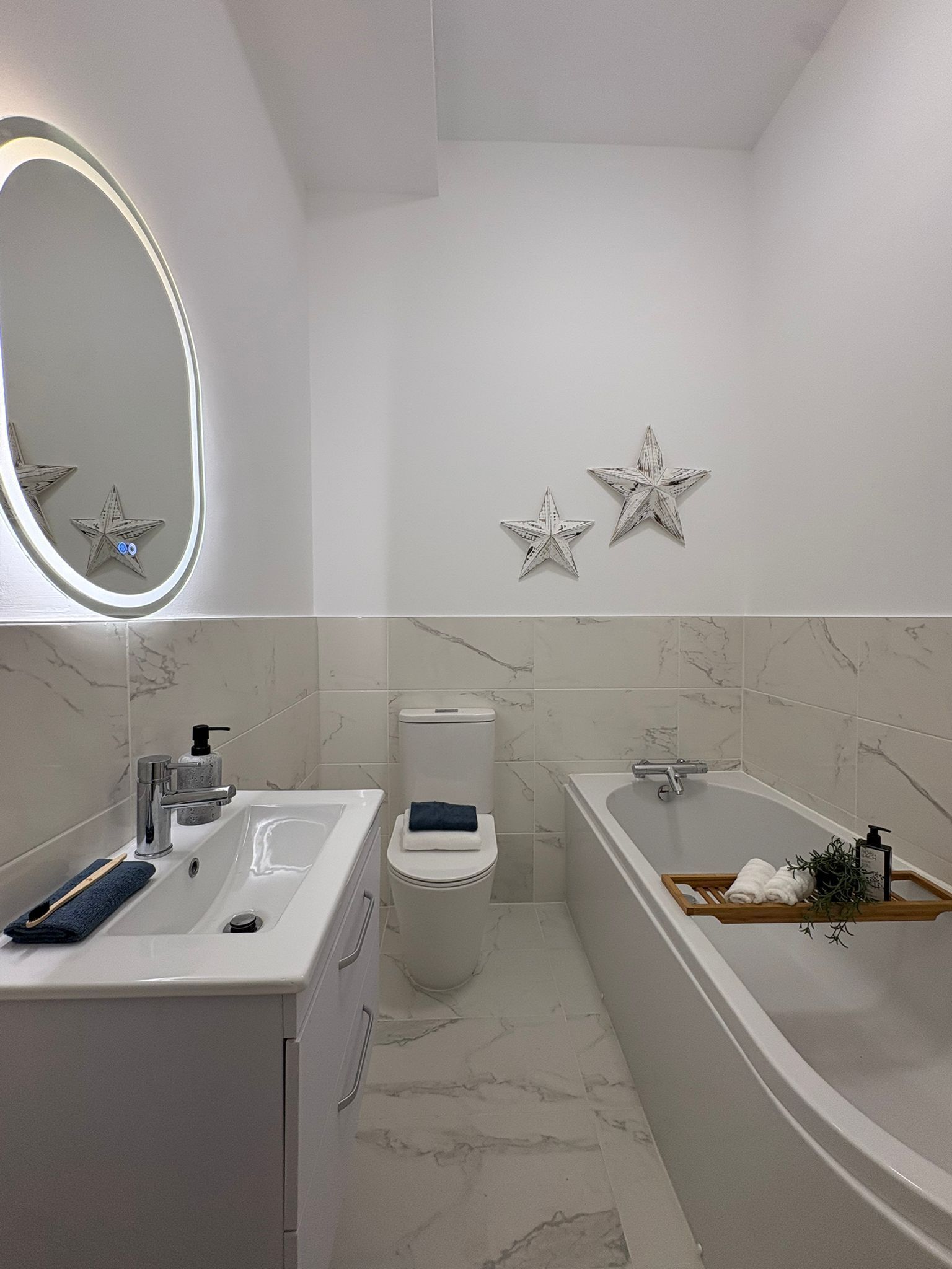 A bathroom with a white sink, toilet, and bathtub. There are two star-shaped wall decorations and a round mirror above the sink.