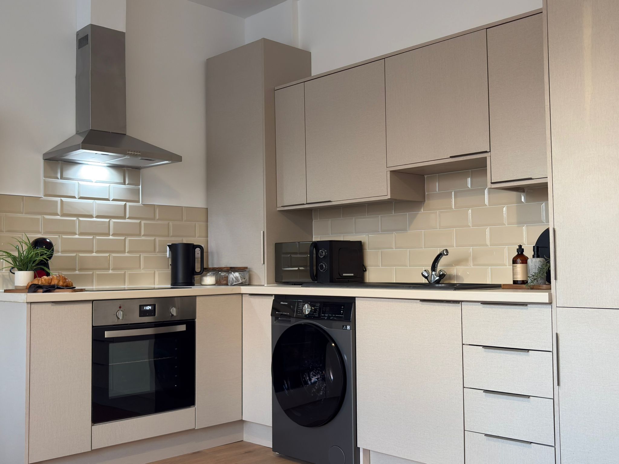 A modern kitchen with a built-in oven, microwave, and dishwasher, featuring light-colored cabinetry and a tiled backsplash.