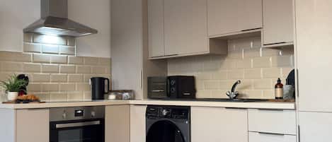 Una cocina moderna con horno integrado, microondas y lavavajillas, con armarios de colores claros y un salpicadero de azulejos.