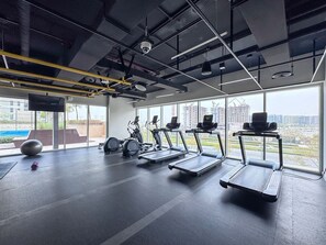 Ein Fitnessraum mit Laufbändern, Ergometer und Rudergerät, großen Fenstern und Blick auf Gebäude.