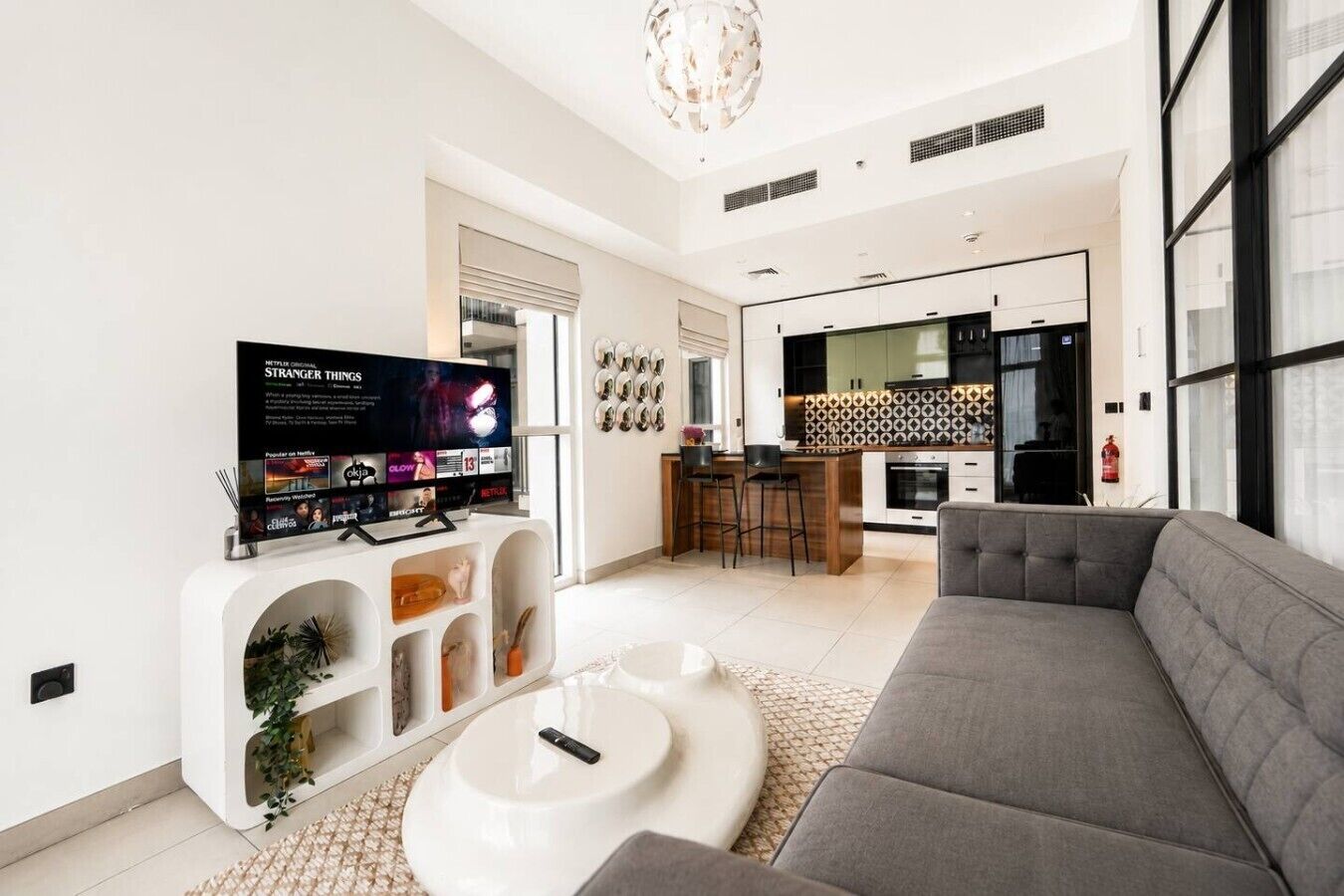 Uma sala de estar moderna com uma TV de tela plana, um sofá cinza e uma mesa de centro.