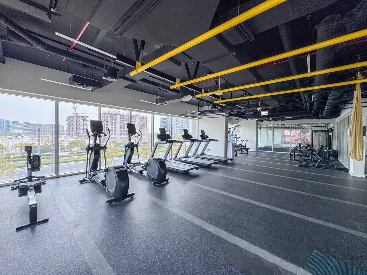 Une salle de sport équipée de matériel d’exercice, dotée de grandes fenêtres et offrant une vue sur les bâtiments.