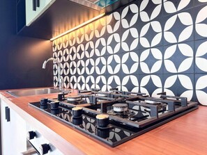 A kitchen with a gas stove, a stainless steel sink, and a patterned backsplash. - Bright & Stylish 2BR Retreat | Socio Dubai Hills (Dubai)