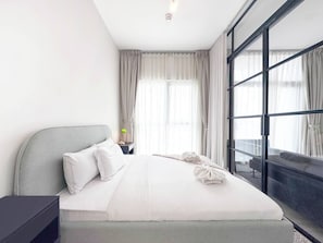 Ein modernes Hotelzimmer mit einem großen Bett, einem Nachttisch, einer Lampe und Blick durch ein großes Fenster.