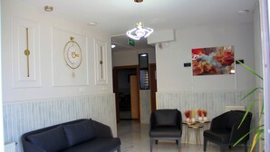 A hotel lobby with a black sofa, two armchairs, a small table with vases, a large abstract painting, and a decorative wall clock.