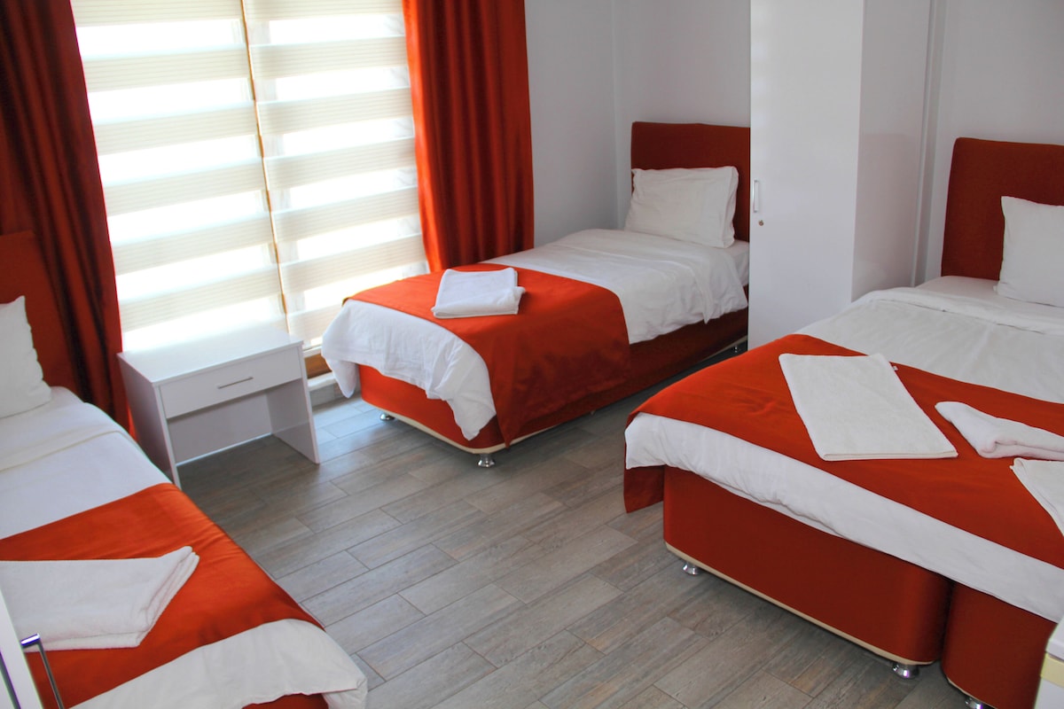 A hotel room with three beds, each with white linens and orange bedding.