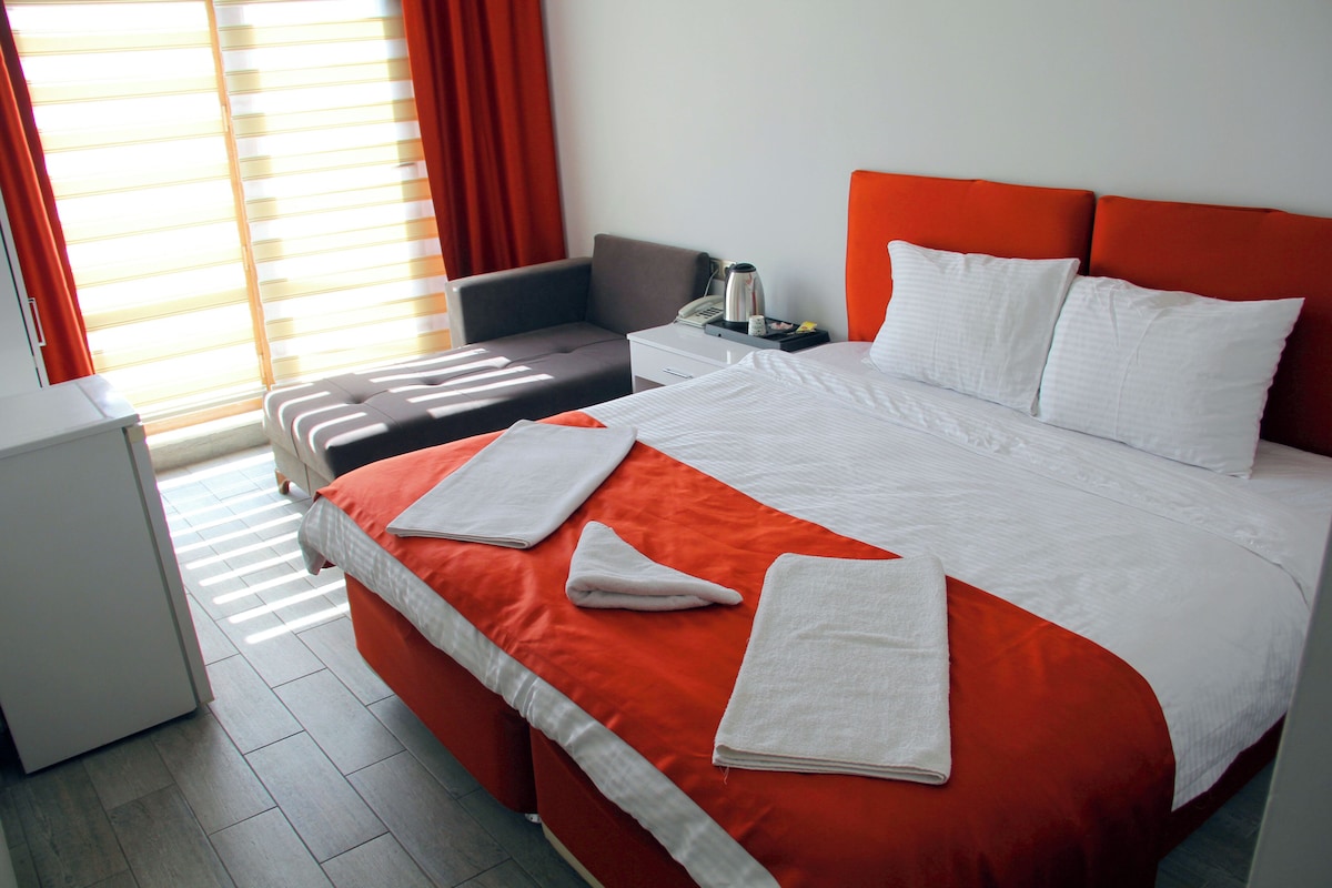A hotel room with a large bed, a desk, a chair, and a window with curtains.