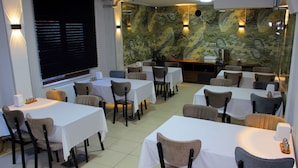 Un restaurante con varias mesas y sillas, una pared de mármol e iluminación instalada en la pared.