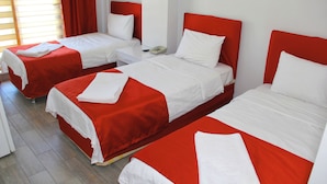 Habitación de hotel con dos camas individuales, cada una con cabecero rojo y ropa de cama blanca. Hay una mesita de noche con un teléfono y una lámpara.