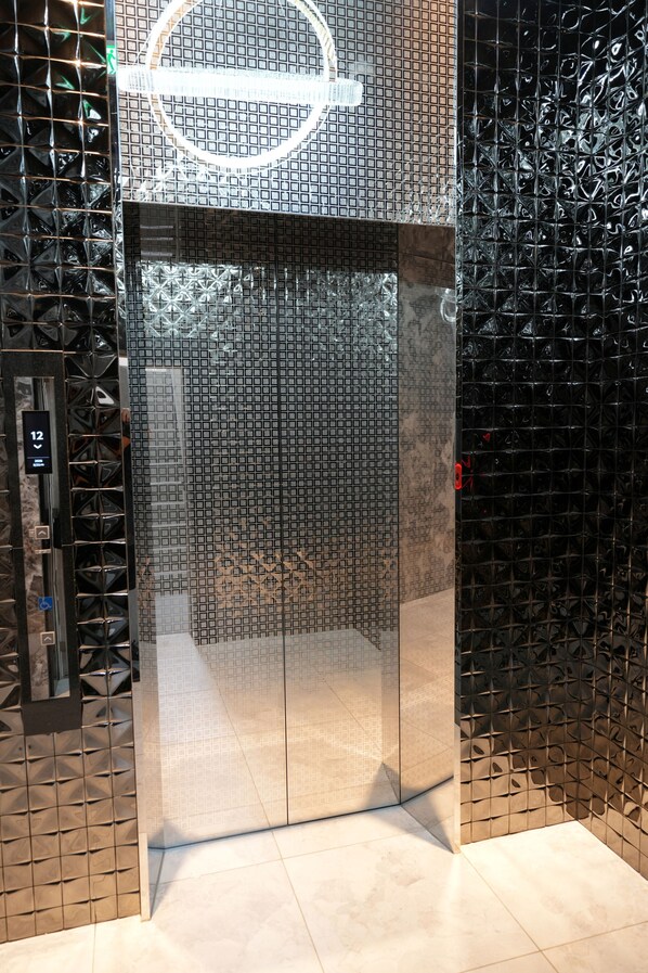Een lift met een glanzend metalen oppervlak en een rond logo bovenaan.