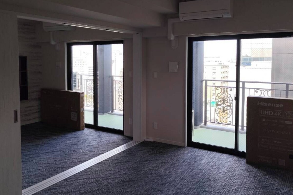A room with a carpeted floor, a sliding glass door leading to a balcony, and an air conditioning unit on the wall.