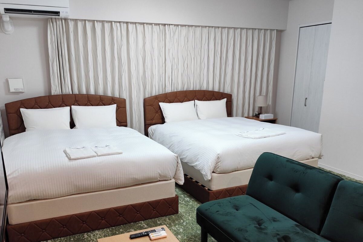 A hotel room with two beds, a green sofa, a wooden coffee table, and a ceiling light.