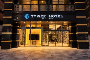 Exterior do Tower Hotel com fachada moderna, ampla entrada de vidro e placa de hotel bem visível.