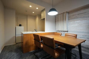 A modern dining area with a wooden table and leather chairs, a built-in kitchen with a refrigerator, and a pendant light above the table. - TOWER HOTEL (Fukuoka)