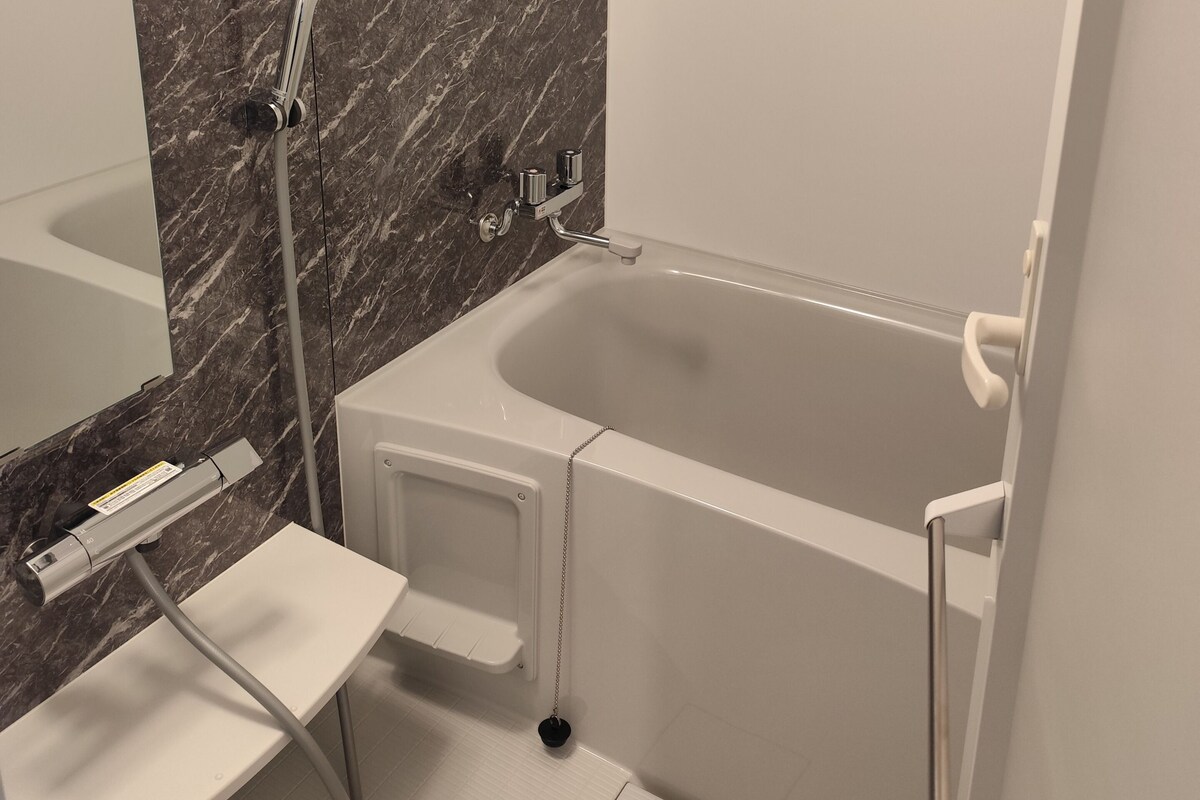 A modern bathroom with a marble wall, a bathtub, a shower, and a white sink.