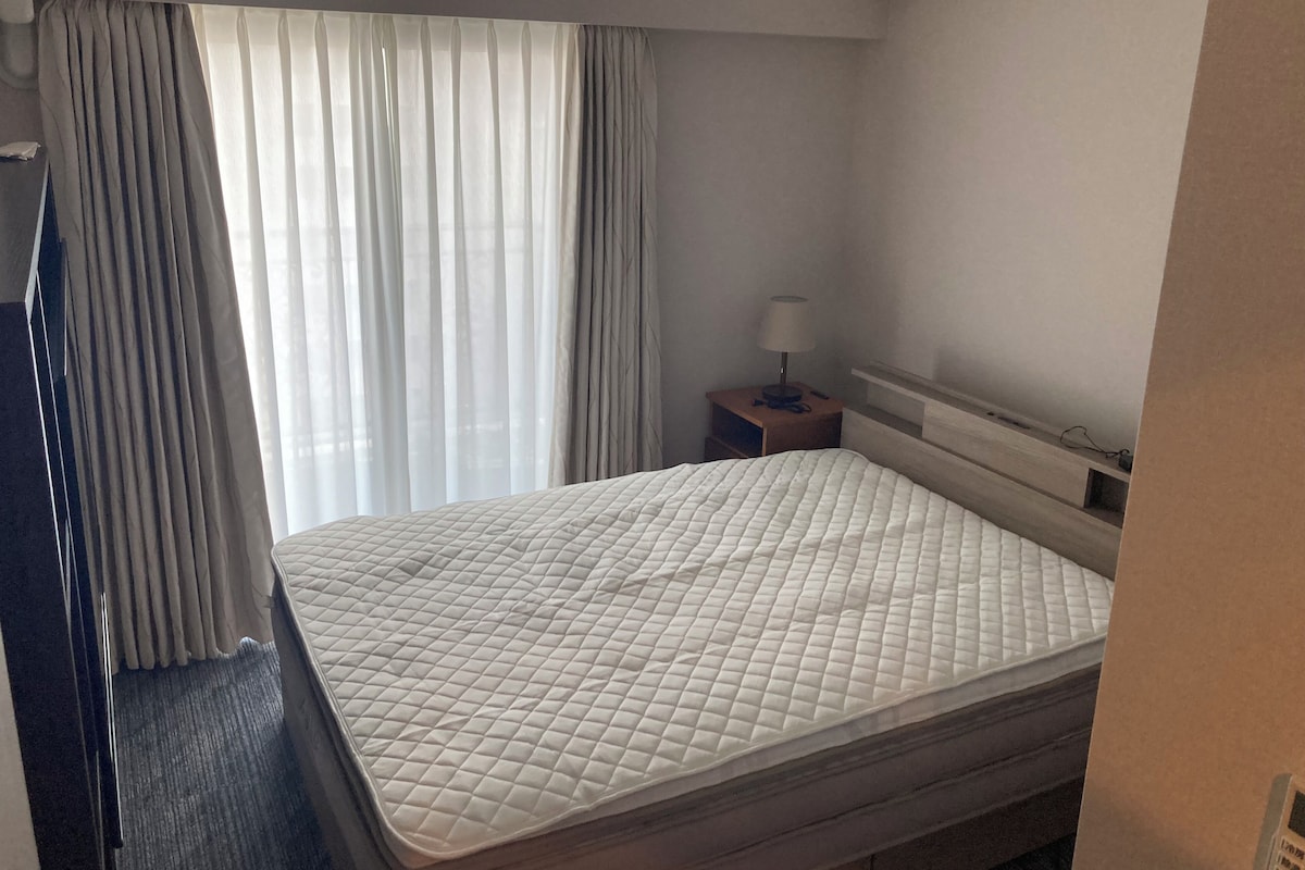 A hotel room with a bed, a nightstand, a lamp, and a window with curtains.