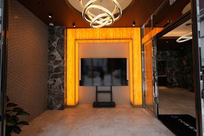 A lobby with a modern interior, a large flat-screen TV mounted on a wall, and a unique circular light fixture above it. - TOWER HOTEL (Fukuoka)
