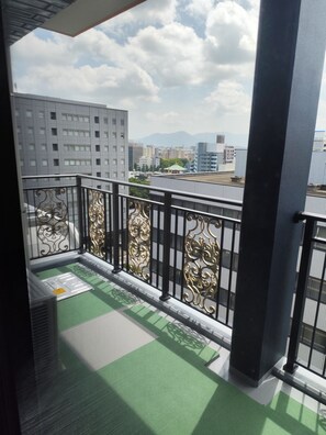 A balcony with ornate black railings, a green mat, and a view of city buildings and mountains in the distance. - TOWER HOTEL (FUKUOKASHI/HAKATAKU/REISENMACHI)