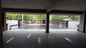 Un couloir intérieur doté d’un sol carrelé, de piliers en béton et d’une entrée fermée par un portail donnant sur l’extérieur.