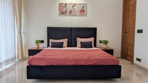 Une chambre à coucher avec un grand lit, deux tables de chevet ornées de plantes en pot, une tête de lit sombre et trois œuvres d’art encadrées accrochées au mur.