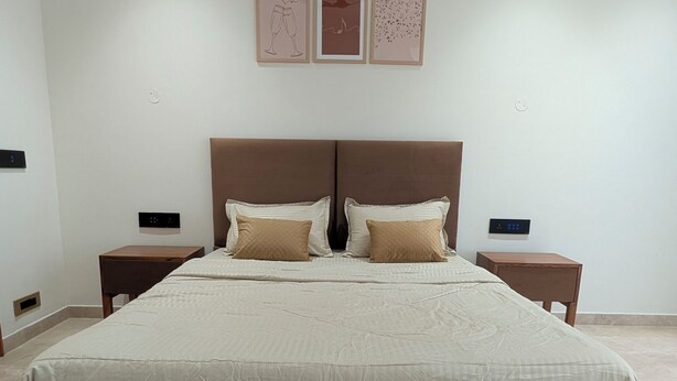 Un grand lit avec une tête de lit, deux tables de chevet et trois tableaux encadrés accrochés au mur.