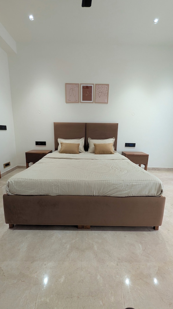 Un grand lit avec une tête de lit, deux tables de chevet et trois tableaux encadrés accrochés au mur.