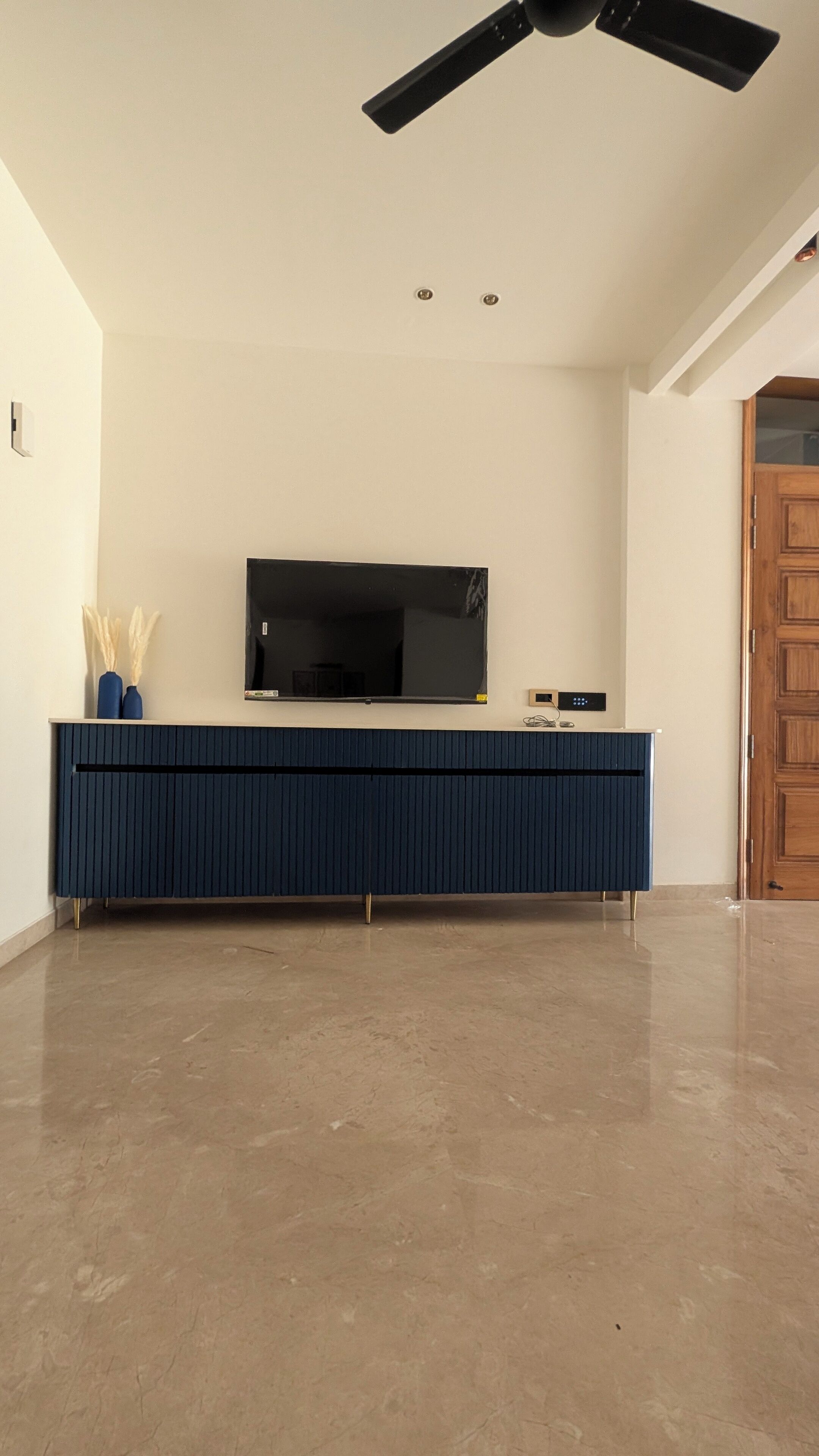 Una habitación con un mueble de entretenimiento azul oscuro, un televisor de pantalla plana montado encima y una puerta de madera a la derecha.