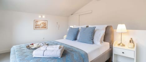 A neatly made bed with a blue and white patterned bedspread, a bedside table with a lamp, and a framed picture on the wall.