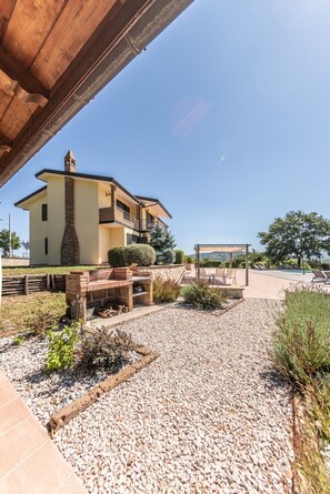 A two-story house with a stone chimney, a patio with seating, and a pool area.