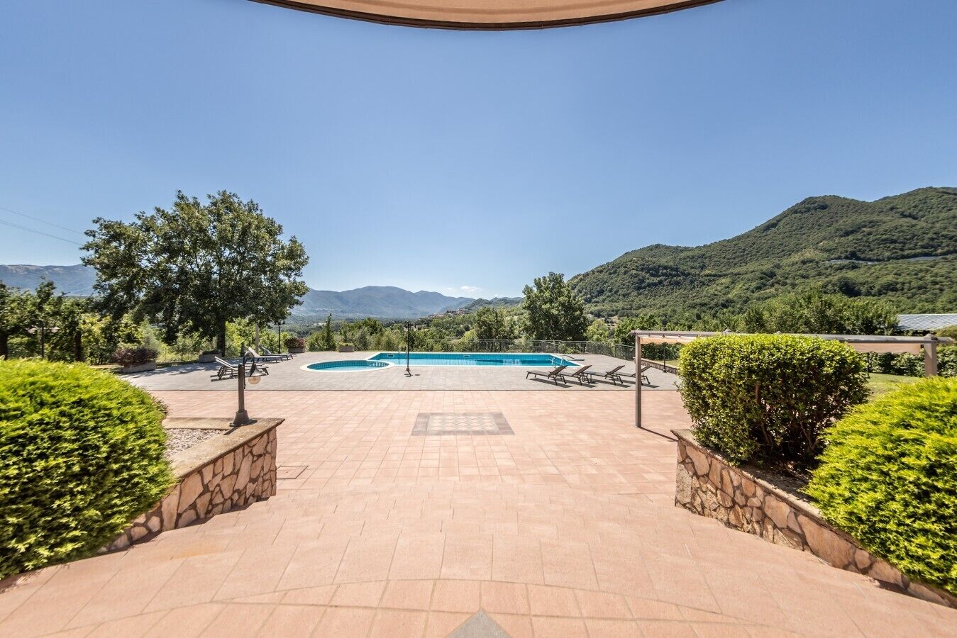 Zona de piscina amb vista a les muntanyes, envoltada de verdura i un cel serè.