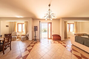 A spacious living area with a dining table, chairs, a sofa, a coat rack, and a chandelier.