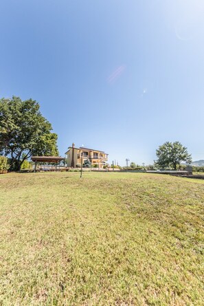 A two-story house with a balcony, surrounded by a grassy field and trees.