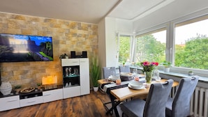 A dining area with a stone wall, a television, and a window with a view of greenery. - Exclusive, bright apartment with balcony in the city, 1 Gbit Wifi, boxspringbeds (Kassel)