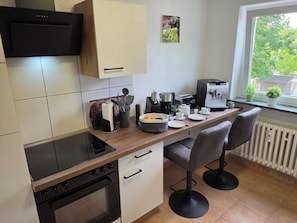 A modern kitchen with a built-in oven, a coffee machine, and two bar stools. - Exclusive, bright apartment with balcony in the city, 1 Gbit Wifi, boxspringbeds (Kassel)