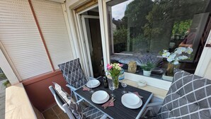 An outdoor dining area with a table set for two, chairs, and a window with a view of the garden. - Exclusive, bright apartment with balcony in the city, 1 Gbit Wifi, boxspringbeds (Kassel)