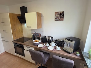 A compact kitchen with a stove, sink, and a coffee machine. There are two chairs and a small table with a plant. - Exclusive, bright apartment with balcony in the city, 1 Gbit Wifi, boxspringbeds (Kassel)