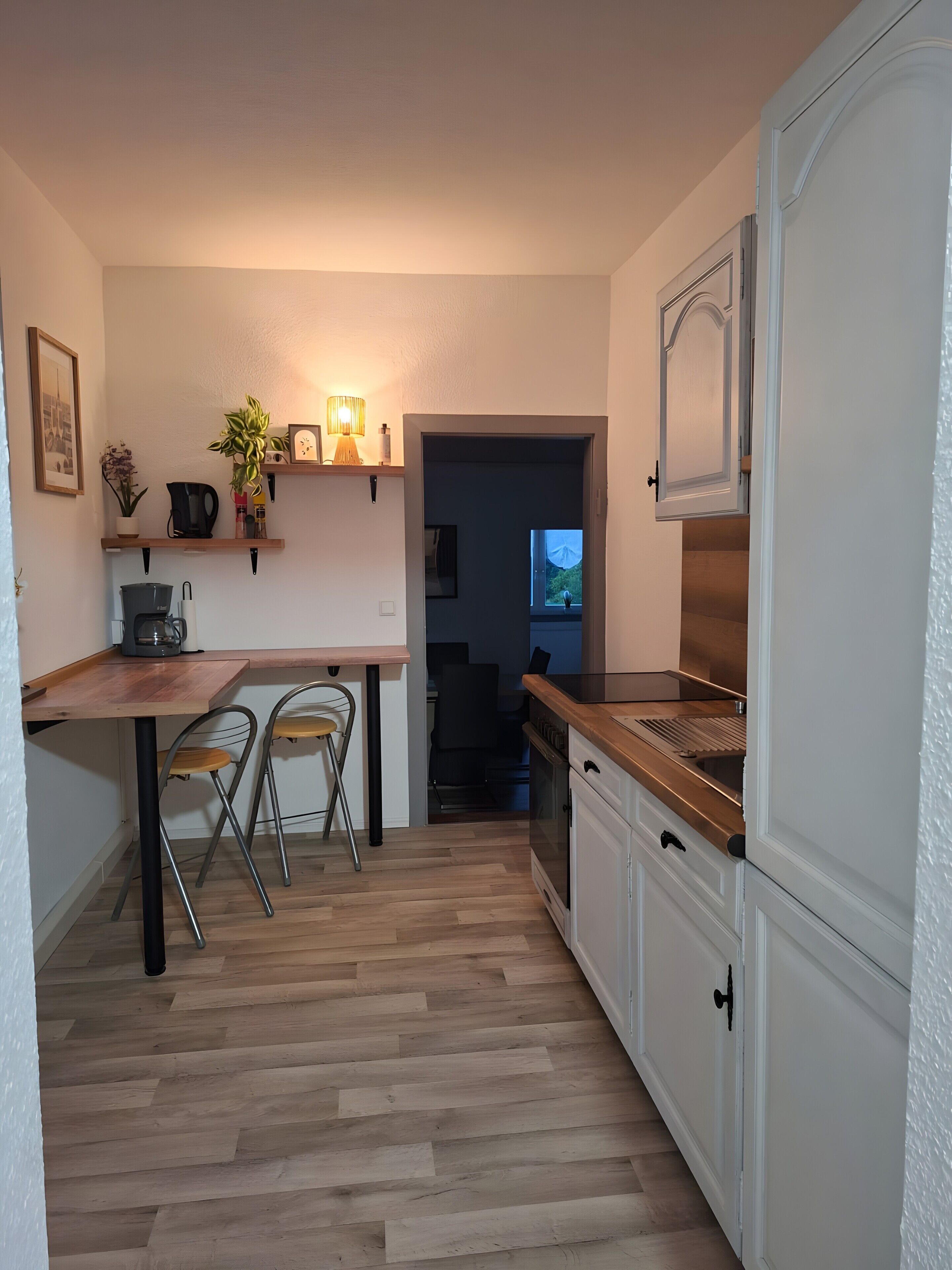 Una cucina compatta con un tavolo di legno, due sedie, una moka e un frigorifero.